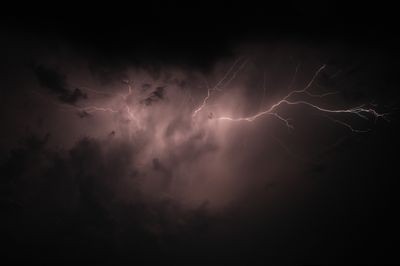 Horizontal lightning strike with a pink hue surrounded by the night sky. The lightning strike comes out from the middle and splits into multiple branches on the right showing different colors.